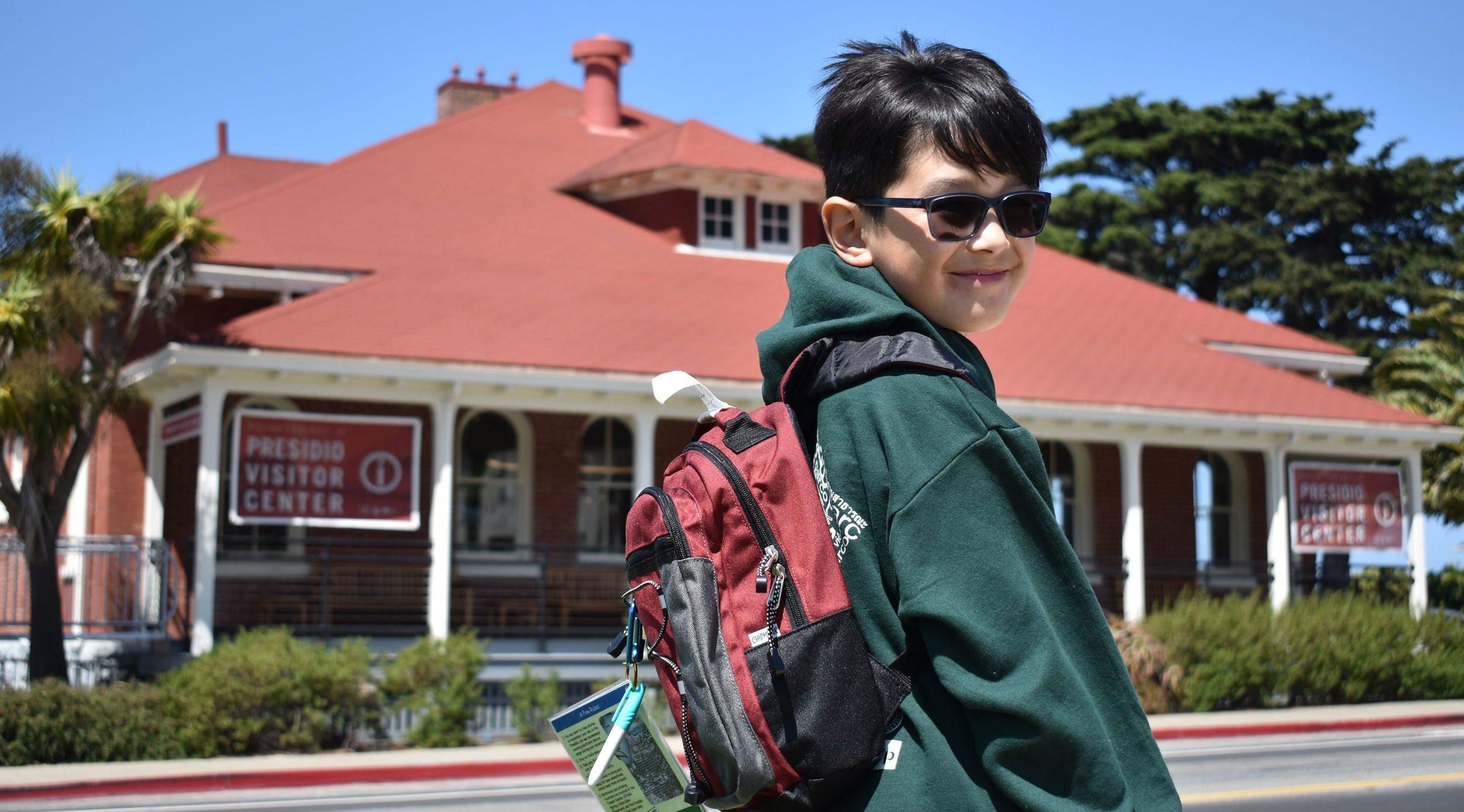 Fisher Tomlinson wearing the red Presidio Explorer Backpack in front of the Presidio Visitor Center