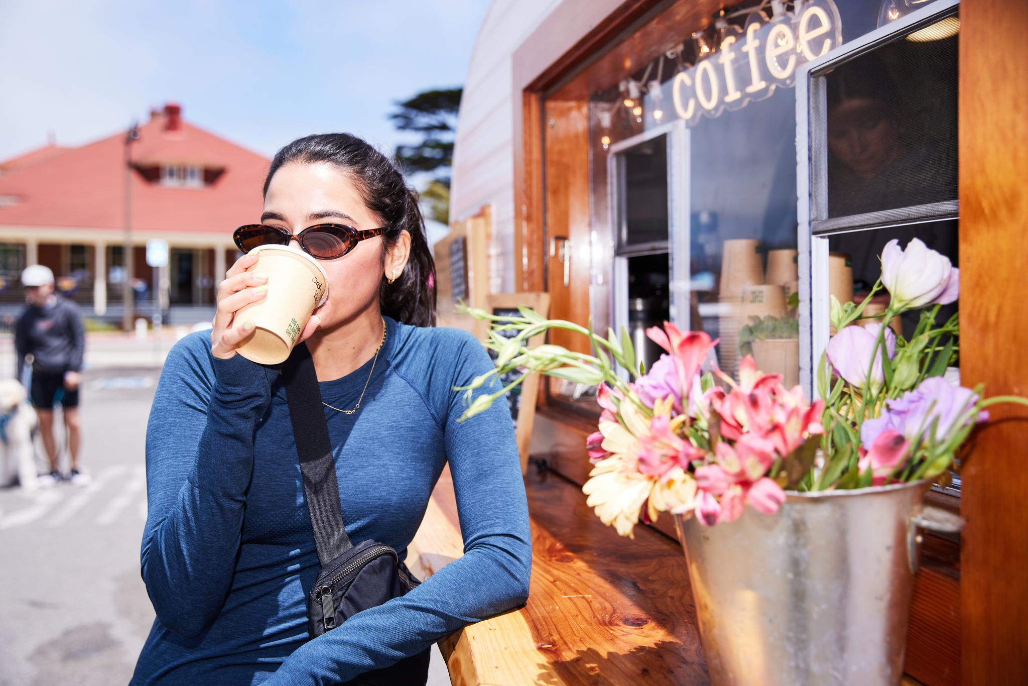 Woman leaning against coffee pop up drinking beverage