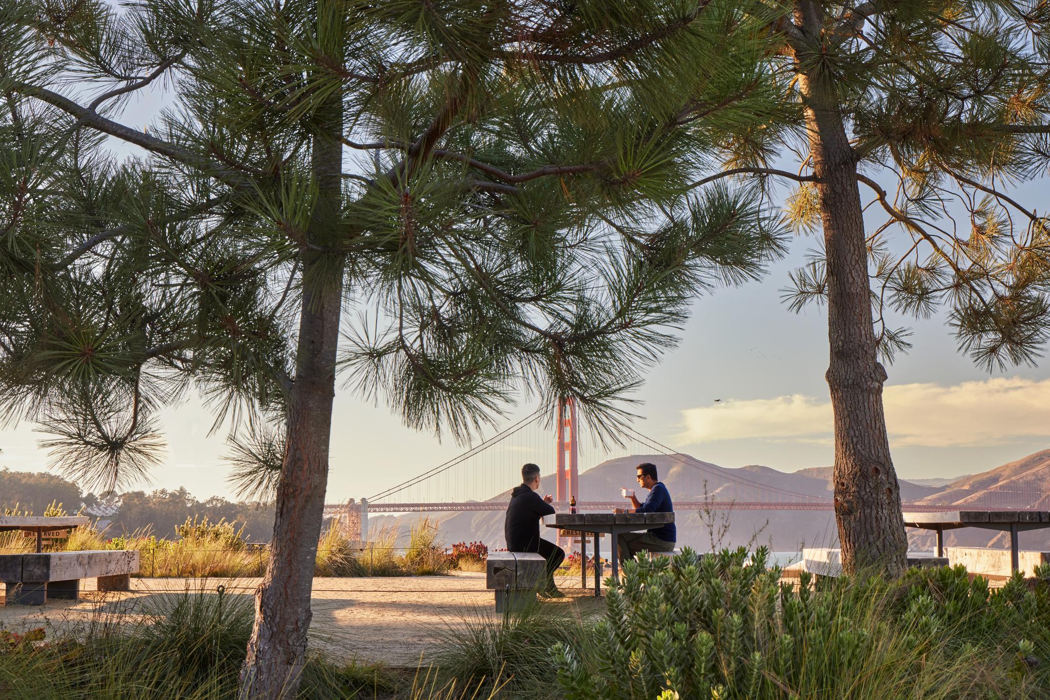 couple sitting at picnic place table at sunset with the golden gate bridge in the background