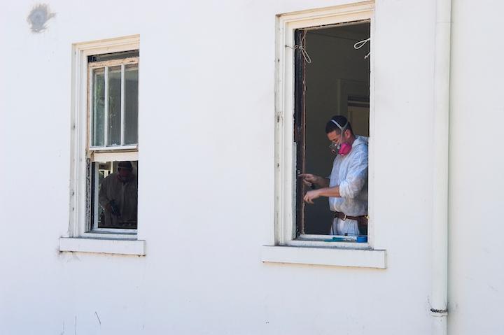 Two workers repair historic windows in a white Presidio building.
