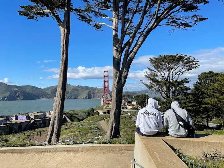 Golden Gate Overlook with two trees framing the bridge and two people sitting on the ledge talking.