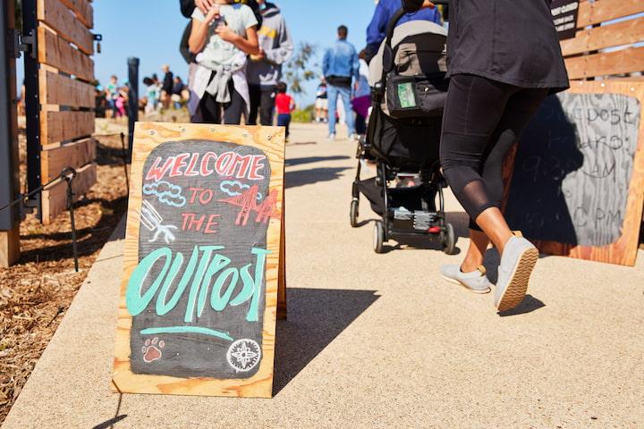 A chalk sign at the entrance to the Outpost, with a stroller nearby.