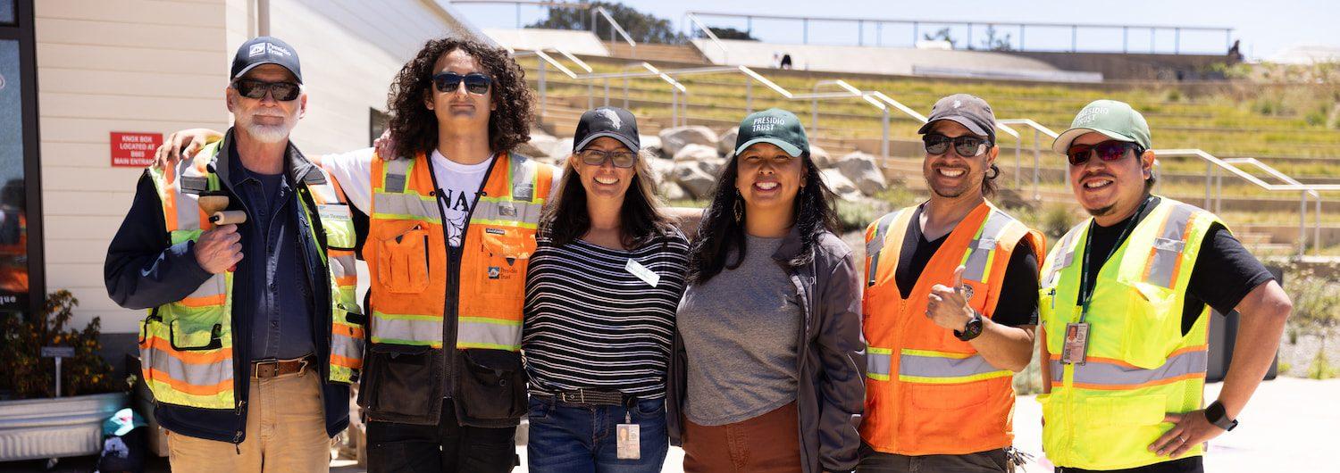 People in construction vests pose in a lot.