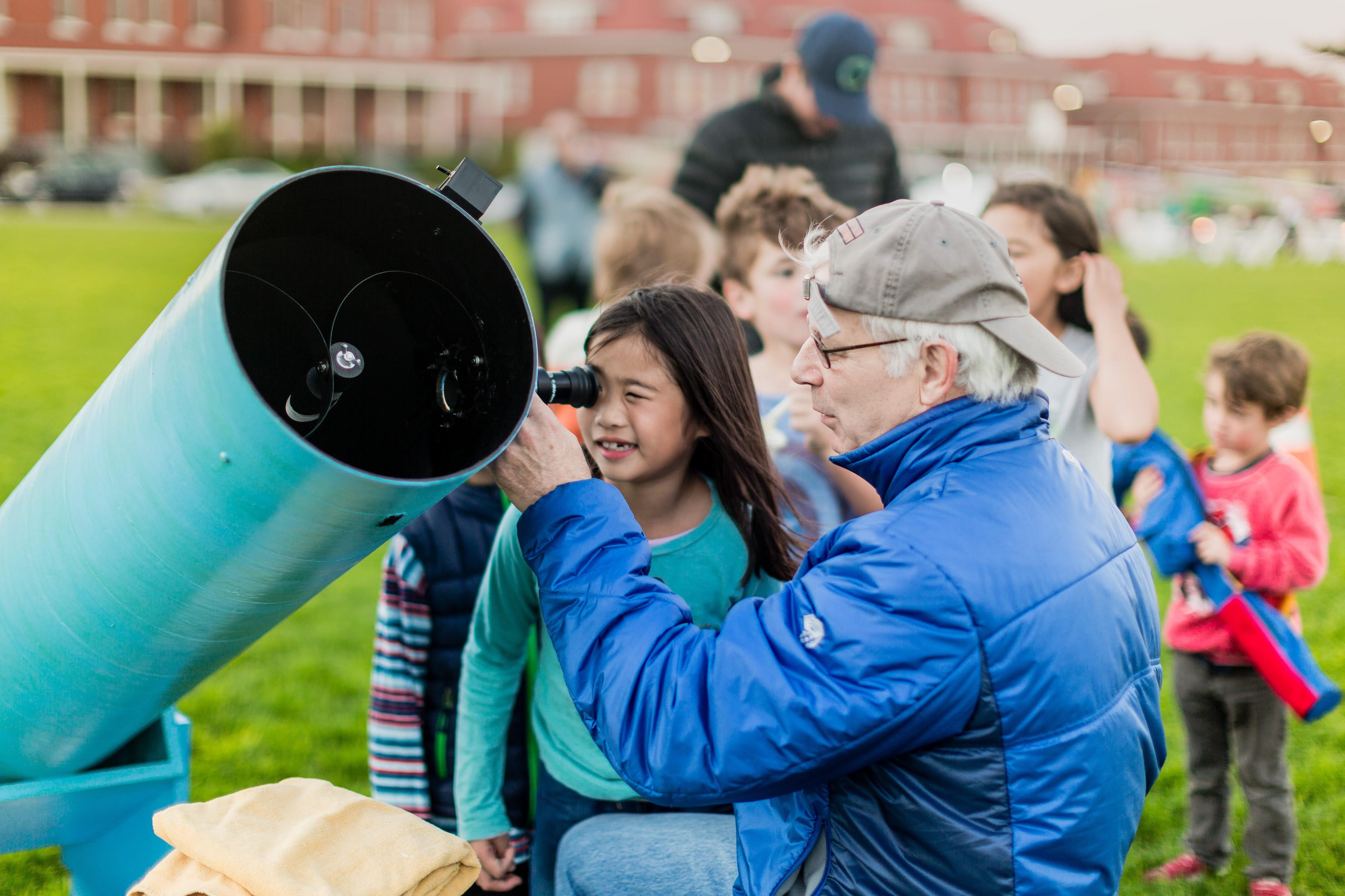 Little girl and man looking into large telescope together.