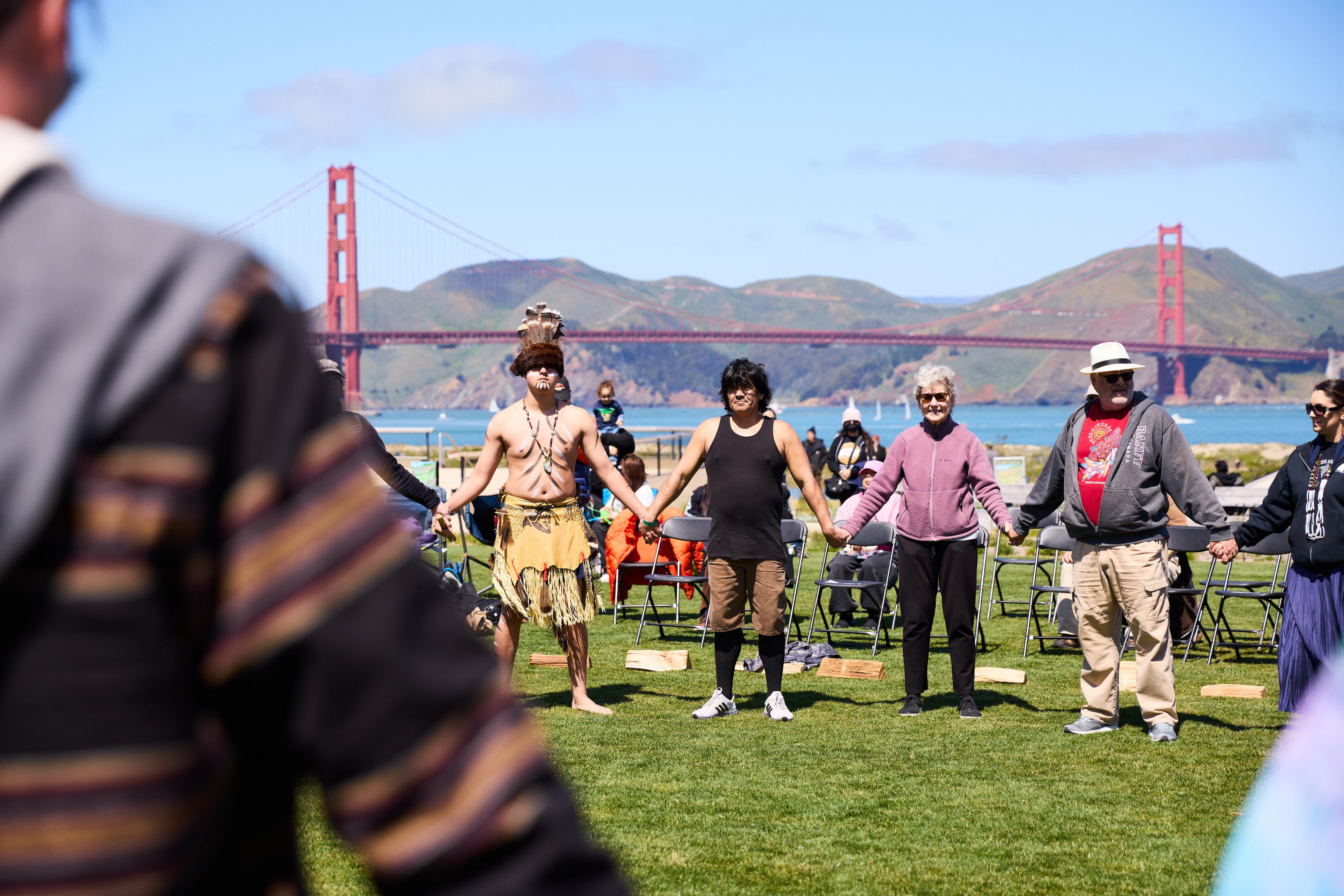 people standing together holding hands with the golden gate bridge in the background
