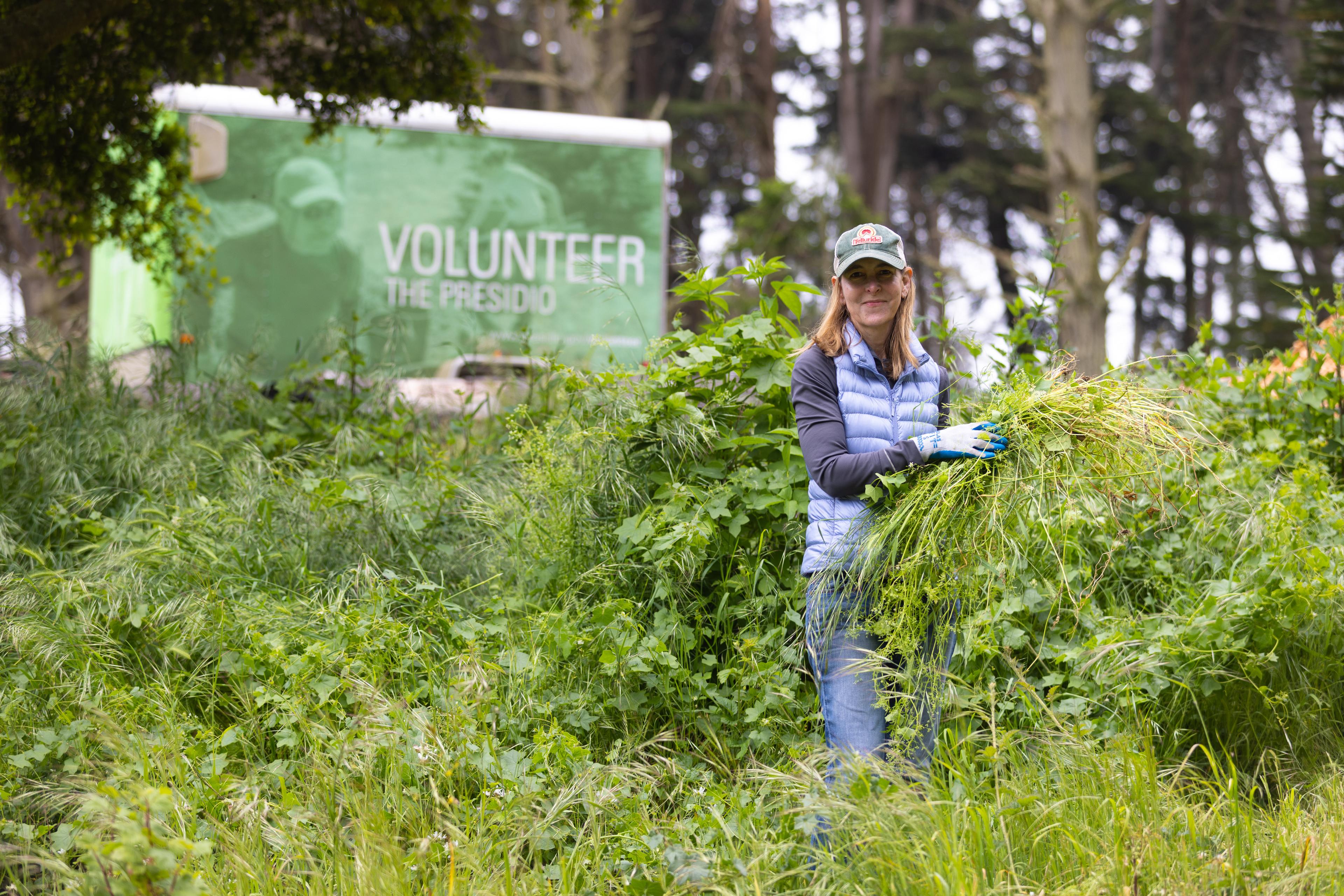 Women holding pile of pulled weeds with a trailer that says Volunteer in the Presidio in the background