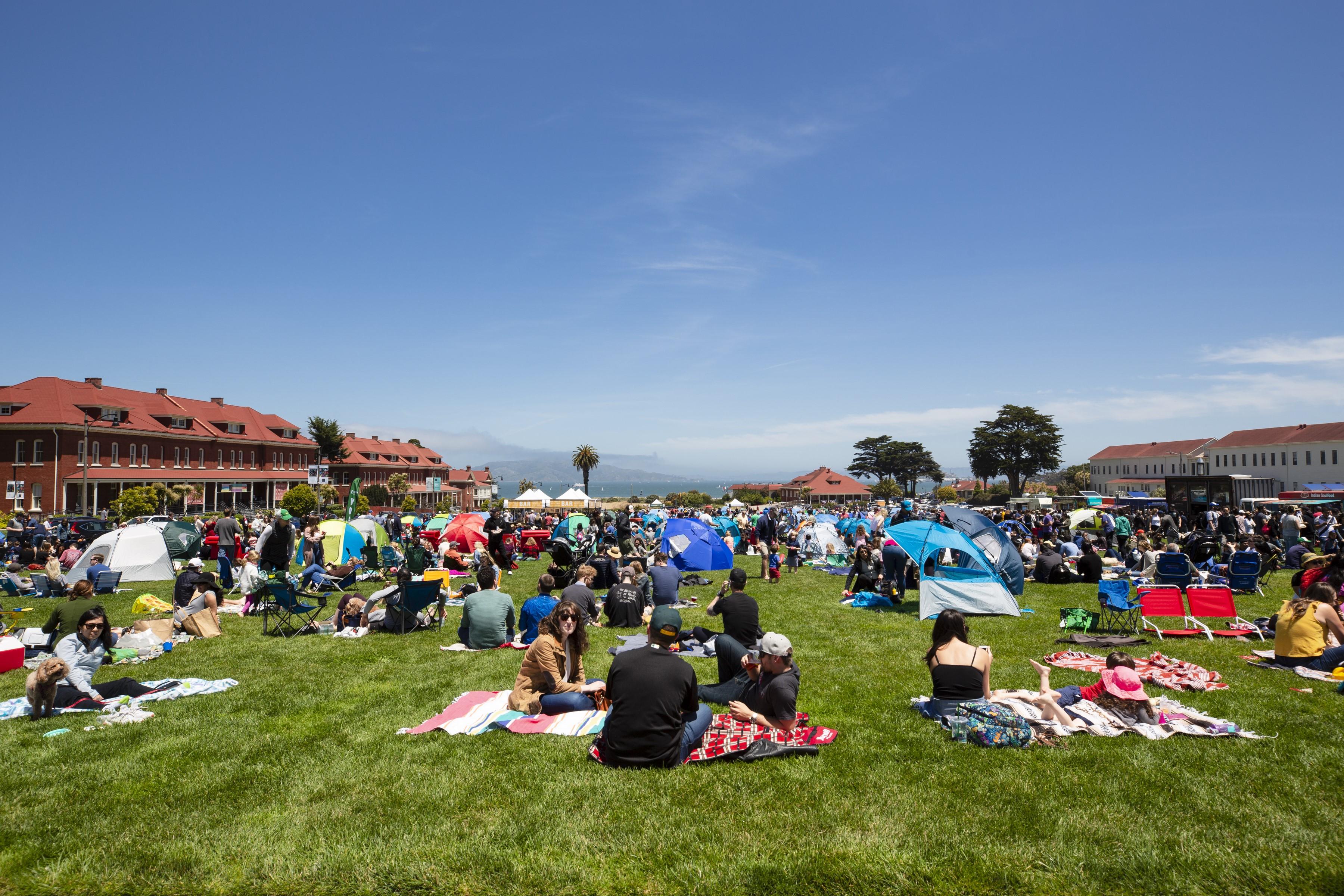 Many people enjoying picnicking and the sun of the Main Lawn at the Presidio of San Francisco.