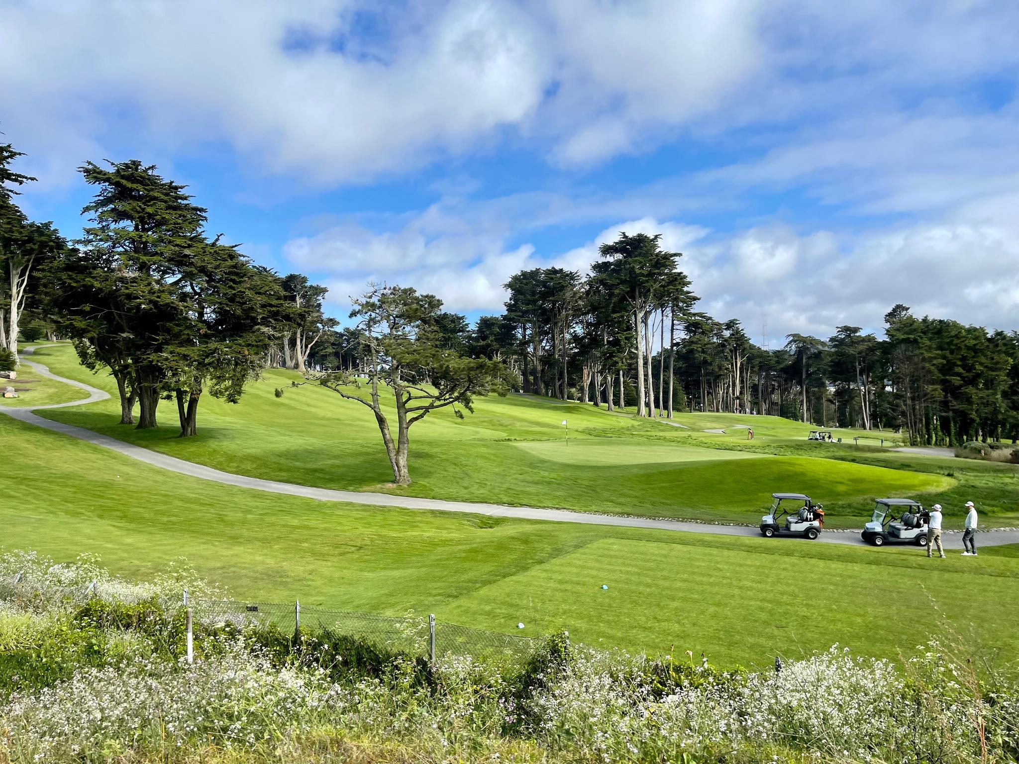 The greens and some golf carts under a cloud-dappled blue sky at Presidio Golf Course.