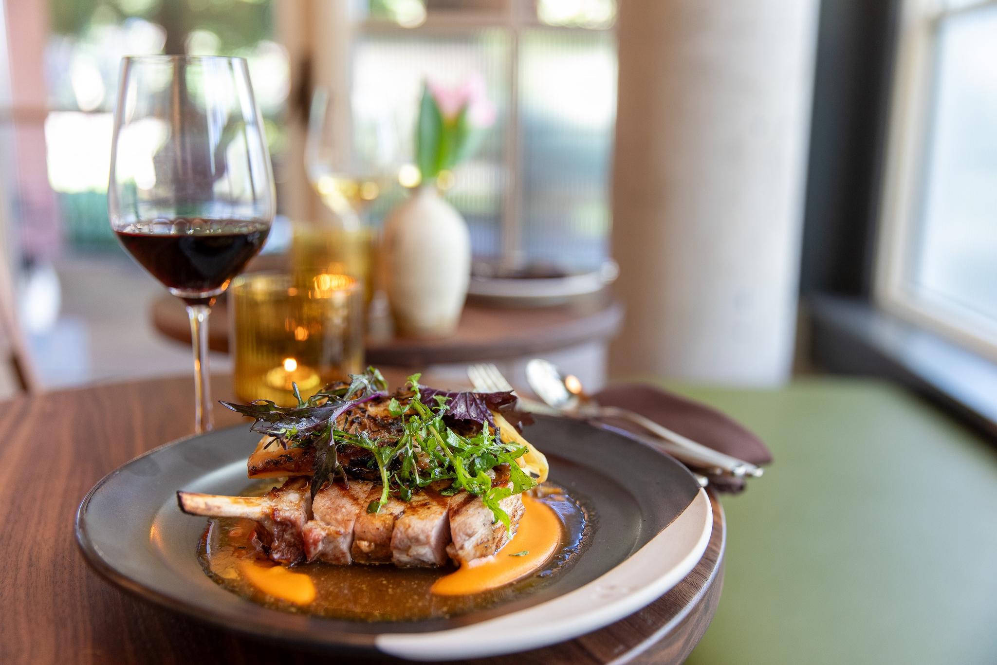 Lamb chops prepared on plate at Piccino Presidio with red wine glass in the background.