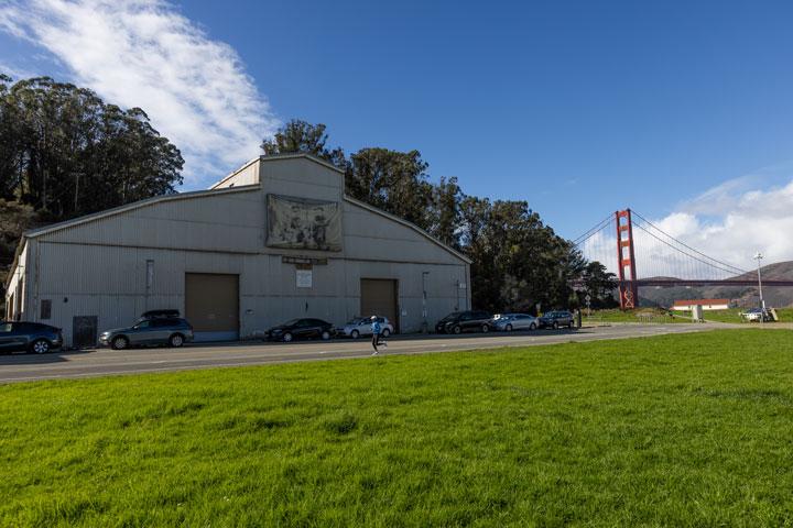 Building 937 exterior by Crissy Field lawn with Golden Gate Bridge in the background.