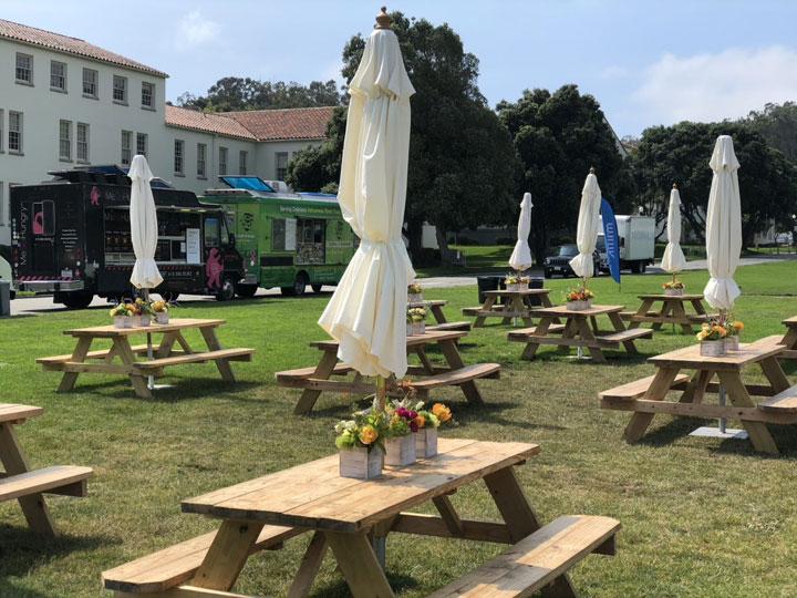 Picnic tables with umbrellas and food trucks for event on Civil War Parade Lawn