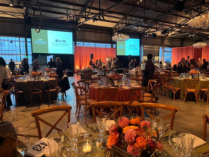 Guests mingling around dining tables while a band is on stage at a fundraising event.