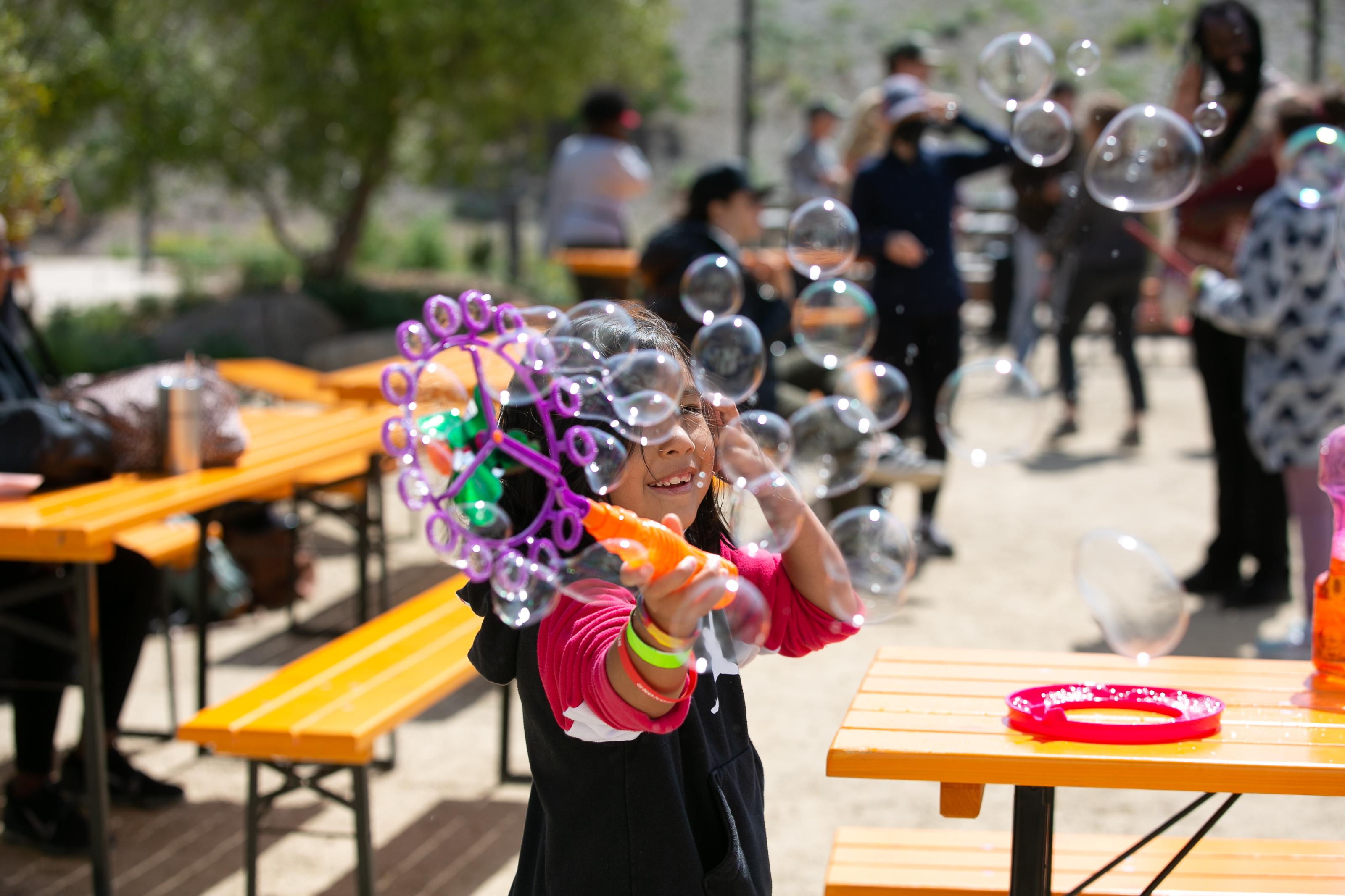 Little girl holding bubbles that are blowing in front of their face