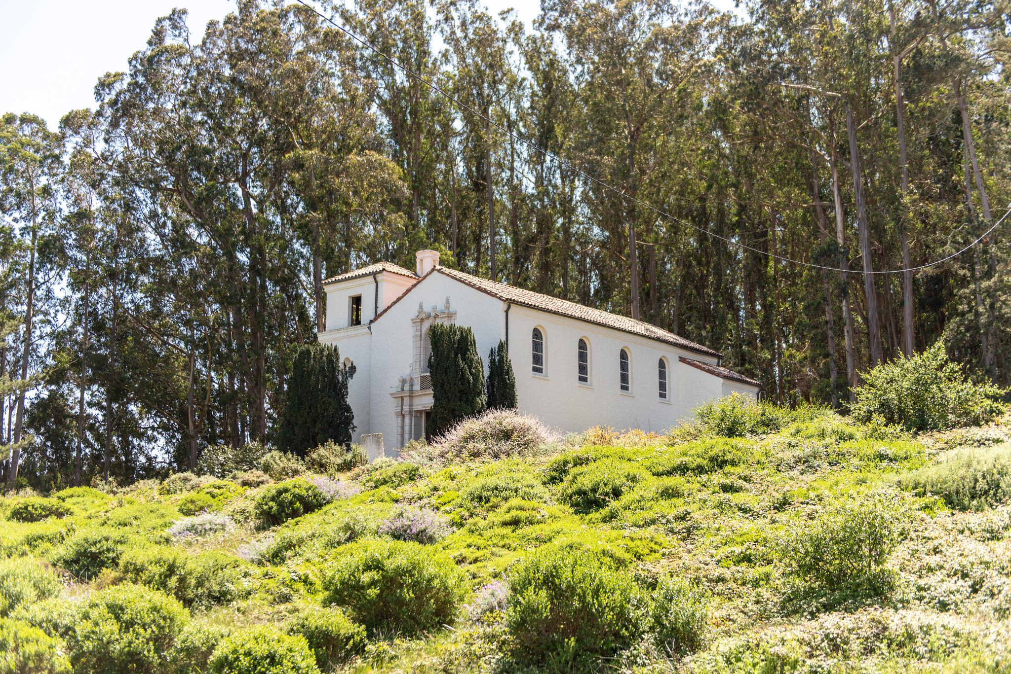 Presidio Chapel exterior from a distance, surrounded by greenery on a sunny day.