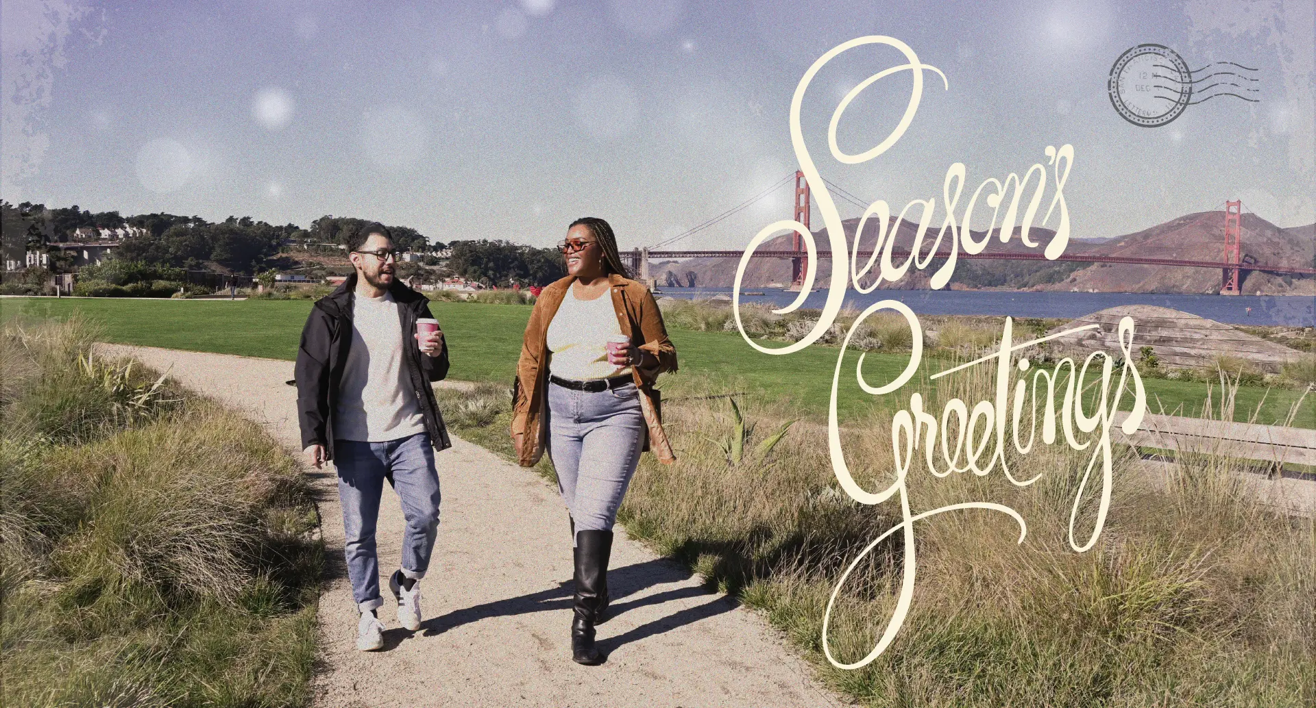 Two people walking at Presidio Tunnel Tops with Golden Gate Bridge in the background and the text, “Seasons Greetings” overhead.