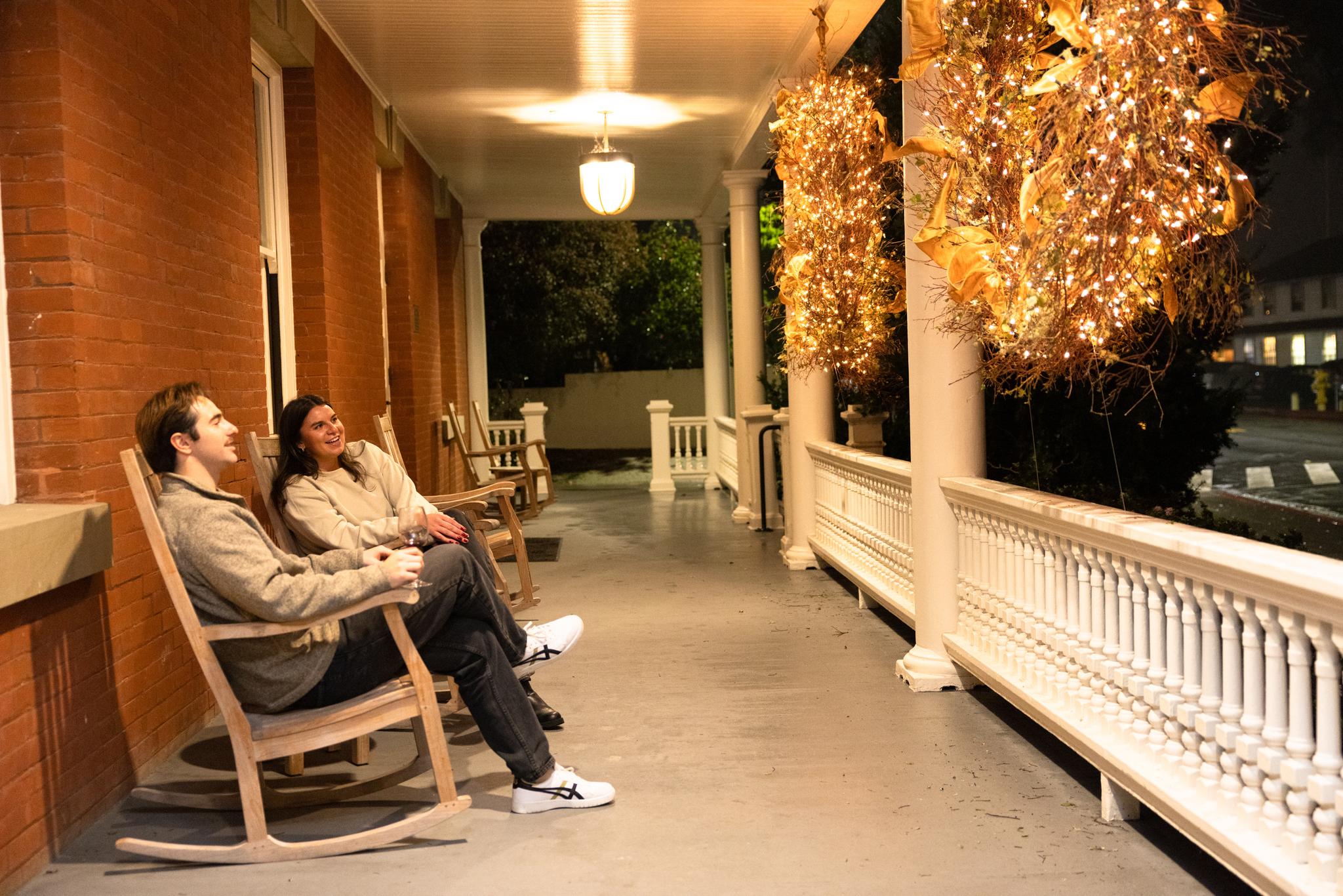 A couple sitting on the porch at the Inn at the Presidio with holiday decorations/wreaths lit.