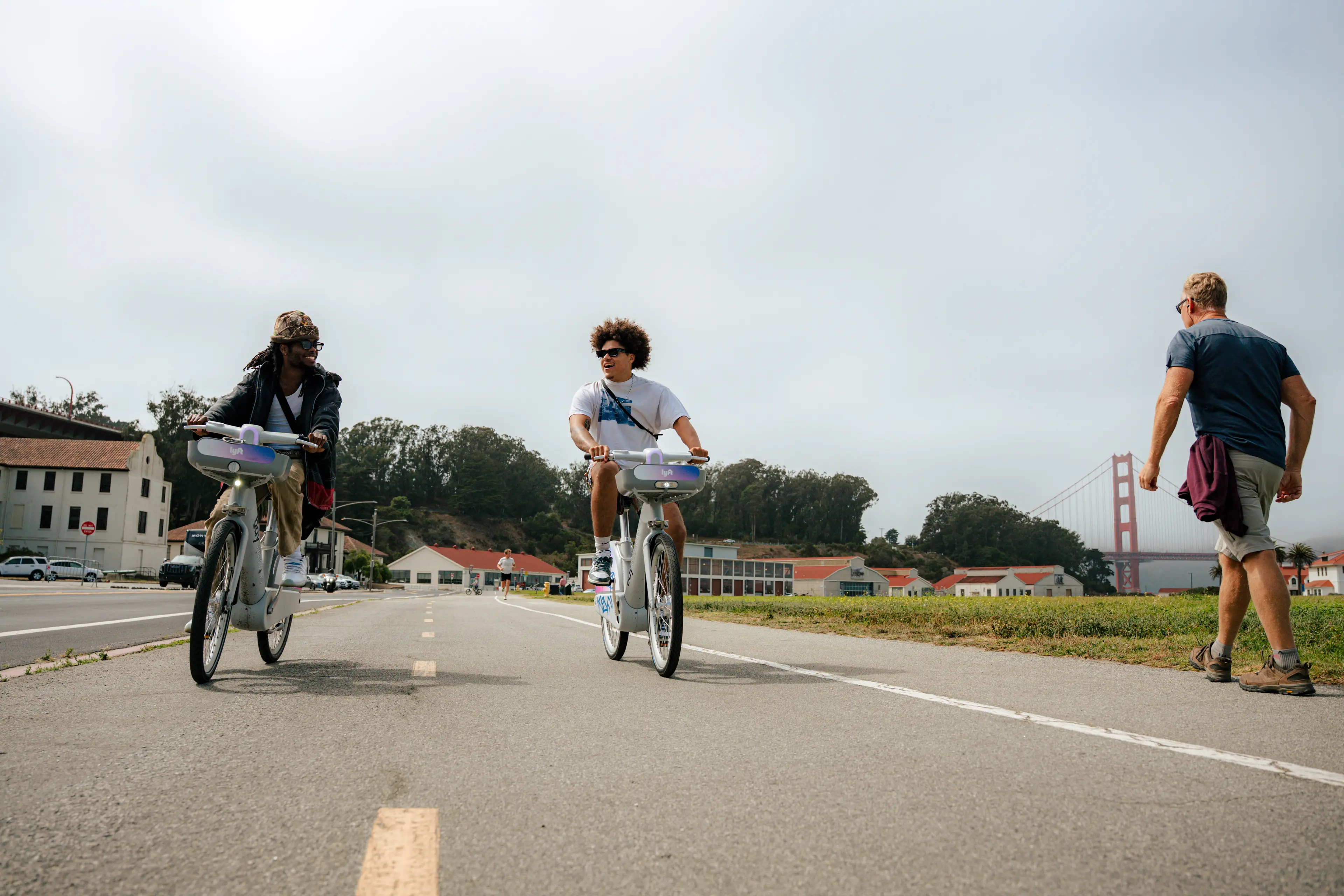 Two people biking next to each other with a man walking beside them with the golden gate bridge in the background,