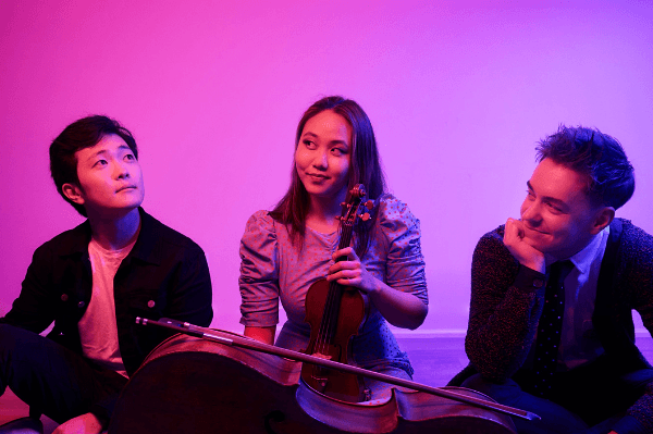 Two men with a woman in the middle and a pinkish purple hue behind them