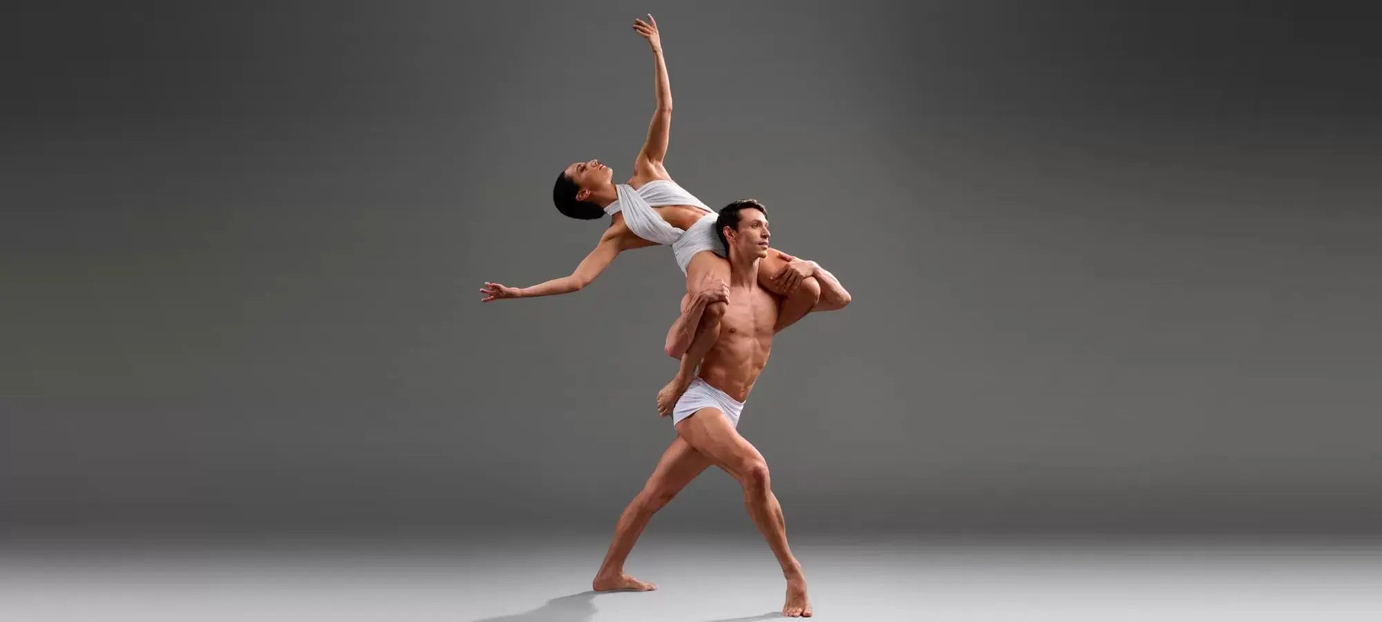 Man hoisting woman above his shoulder in a ballet pose.