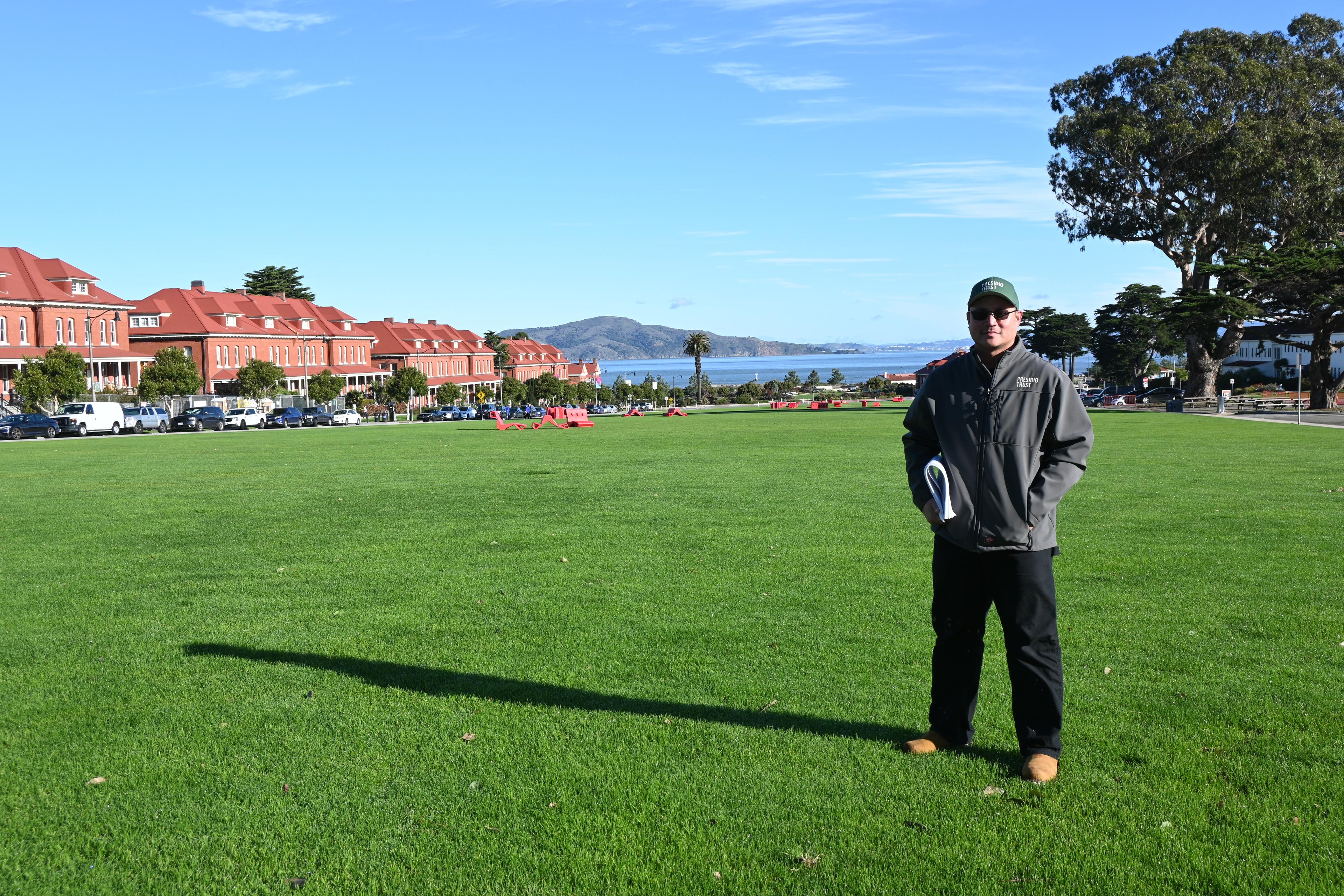 Headshot of Calvin Gee Transportation Project Manager standing on the Presidio's Main Parade Lawn with the bay in the background.