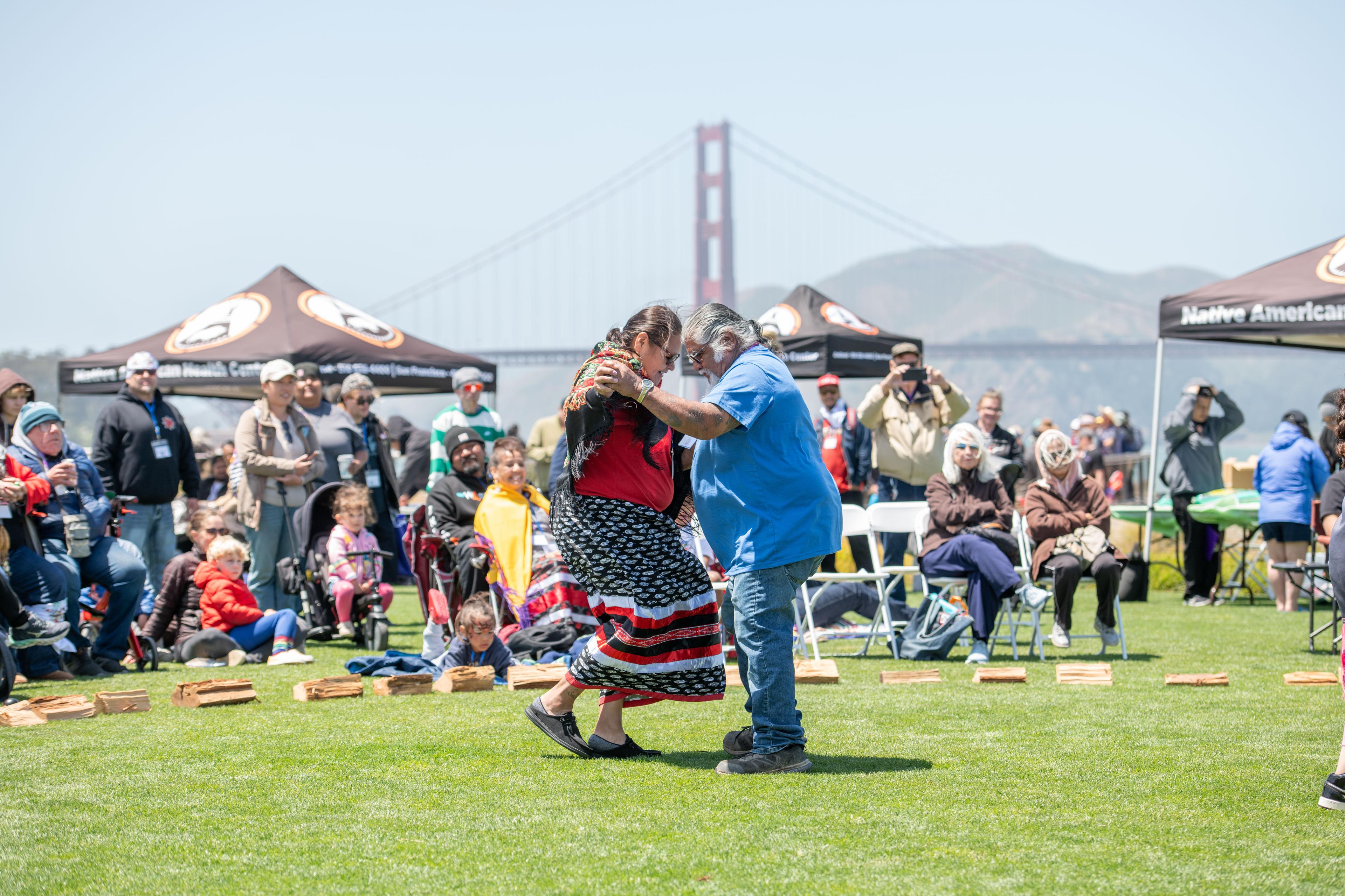 Couple dancing on the Presidio Tunnel Tops in front of a crowd of people with the Golden Gate Bridge in the background