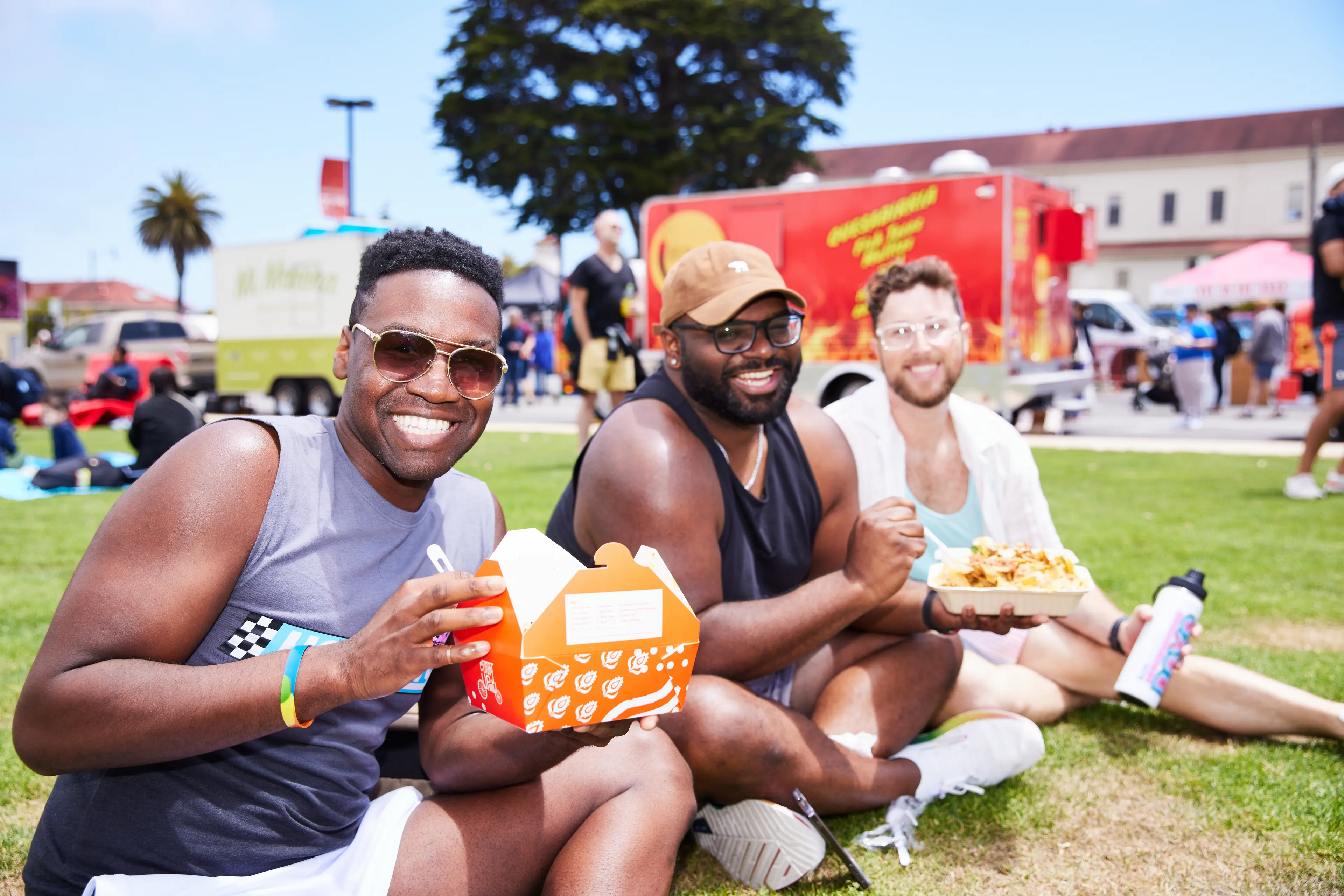 A group of 3 men sitting together on the Presidio Tunnel Tops eating food for the food trucks.