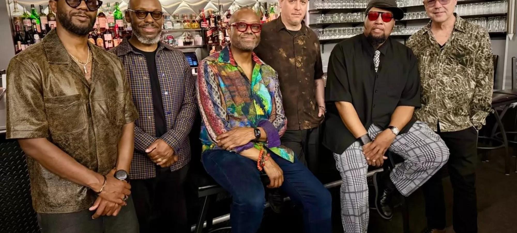 A music group standing and sitting together posing for the photos