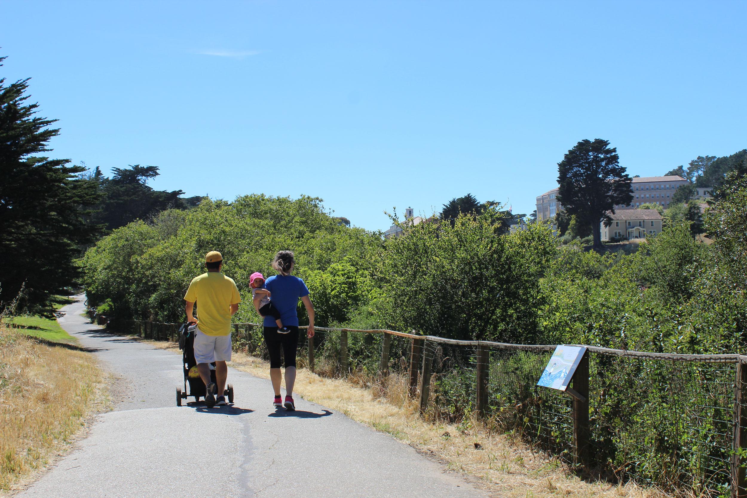 Man with a stroller and woman carrying baby walking down Mountain Lake Trail