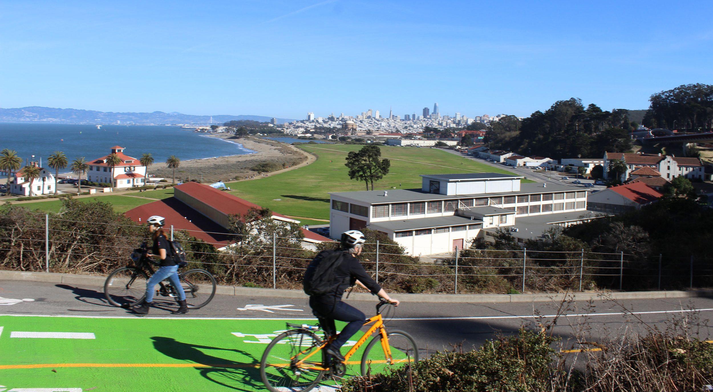 Bicyclists using trail with views of Crissy Field and city skyline in the background.