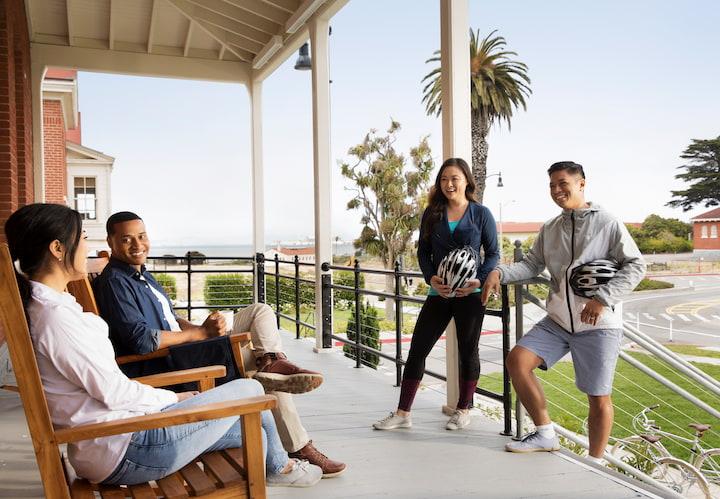 Four people standing and sitting on the porch of the Lodge at the Presidio. Photo by Paul Dyer.