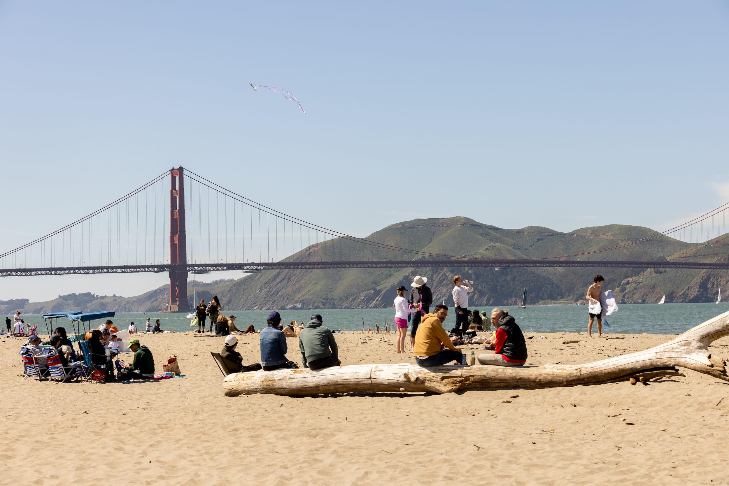 Visitors on the sand at East Beach in the Presidio enjoying the Golden Gate Bridge views.
