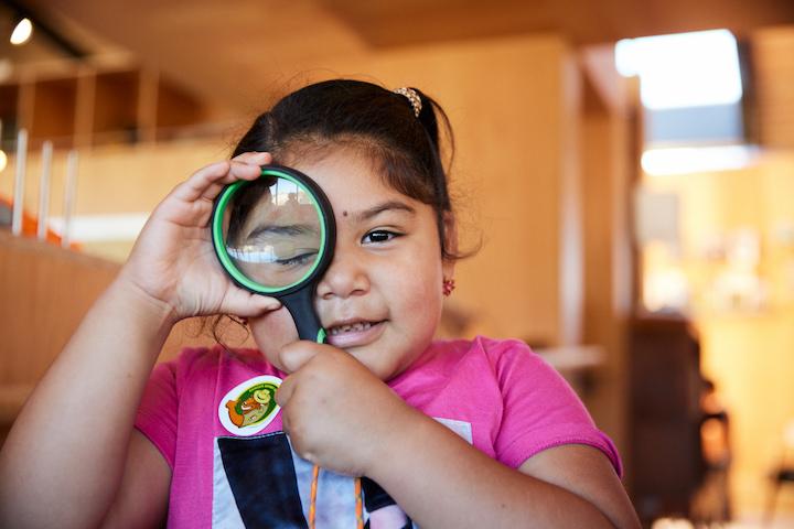 A girl looks through a magnifying glass at the Field Station.