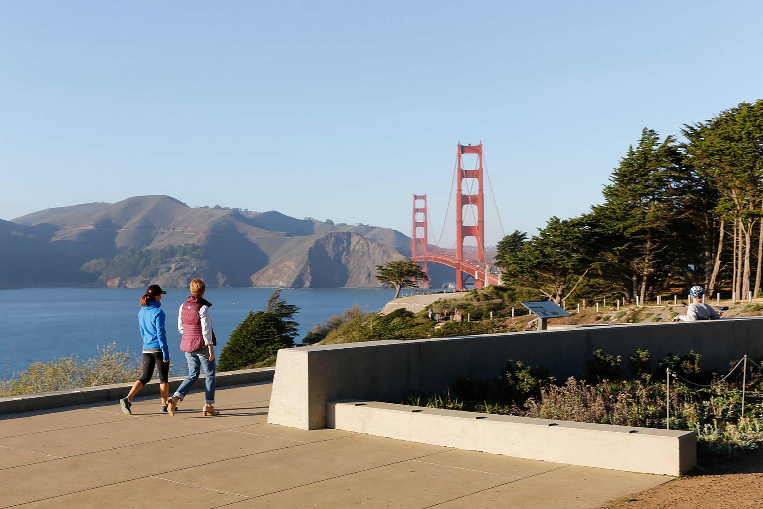 Two women walking at the Pacific Overlook, with the Golden Gate Bridge in the background. Photo by Jay Graham.