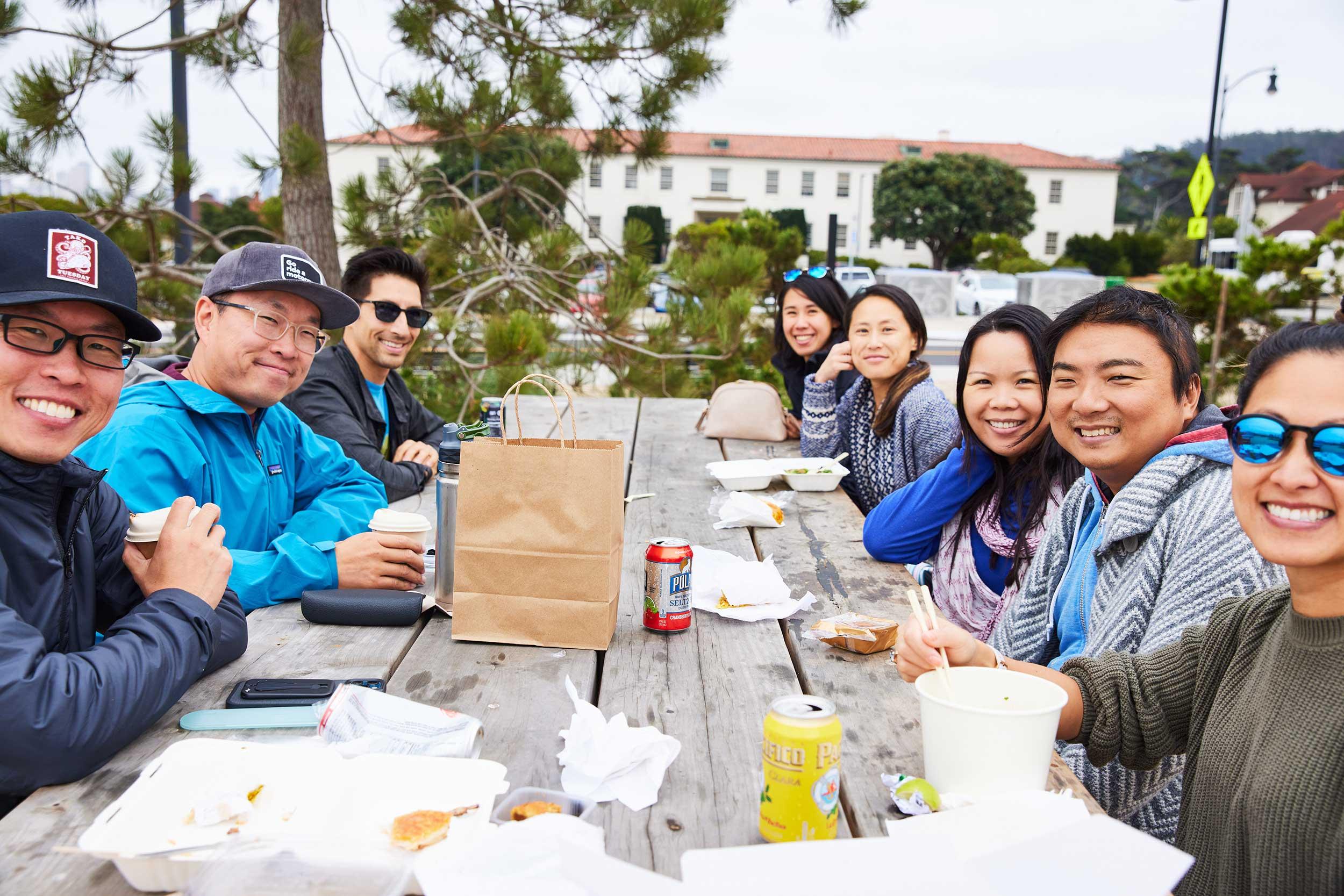A large group of people sitting at a table at Picnic Place in the Presidio. Photo by Rachel Styer.