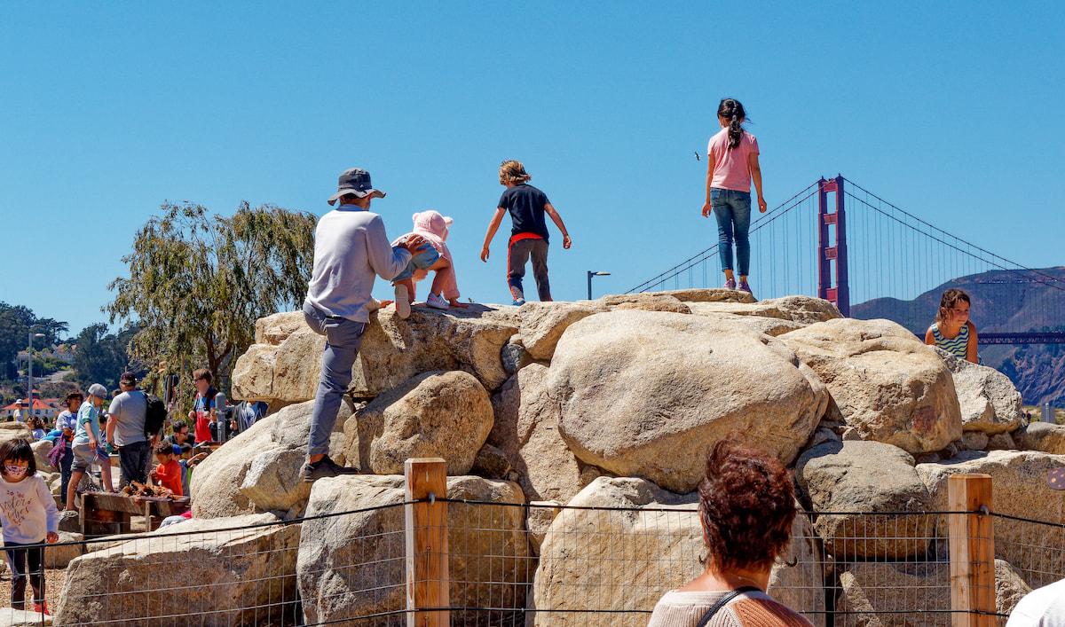 Children on a playground structure made of boulders at the Outpost play space near Crissy Field.