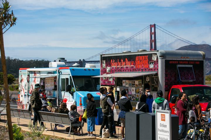 People buying food from two food trucks, with the Golden Gate Bridge in the background.