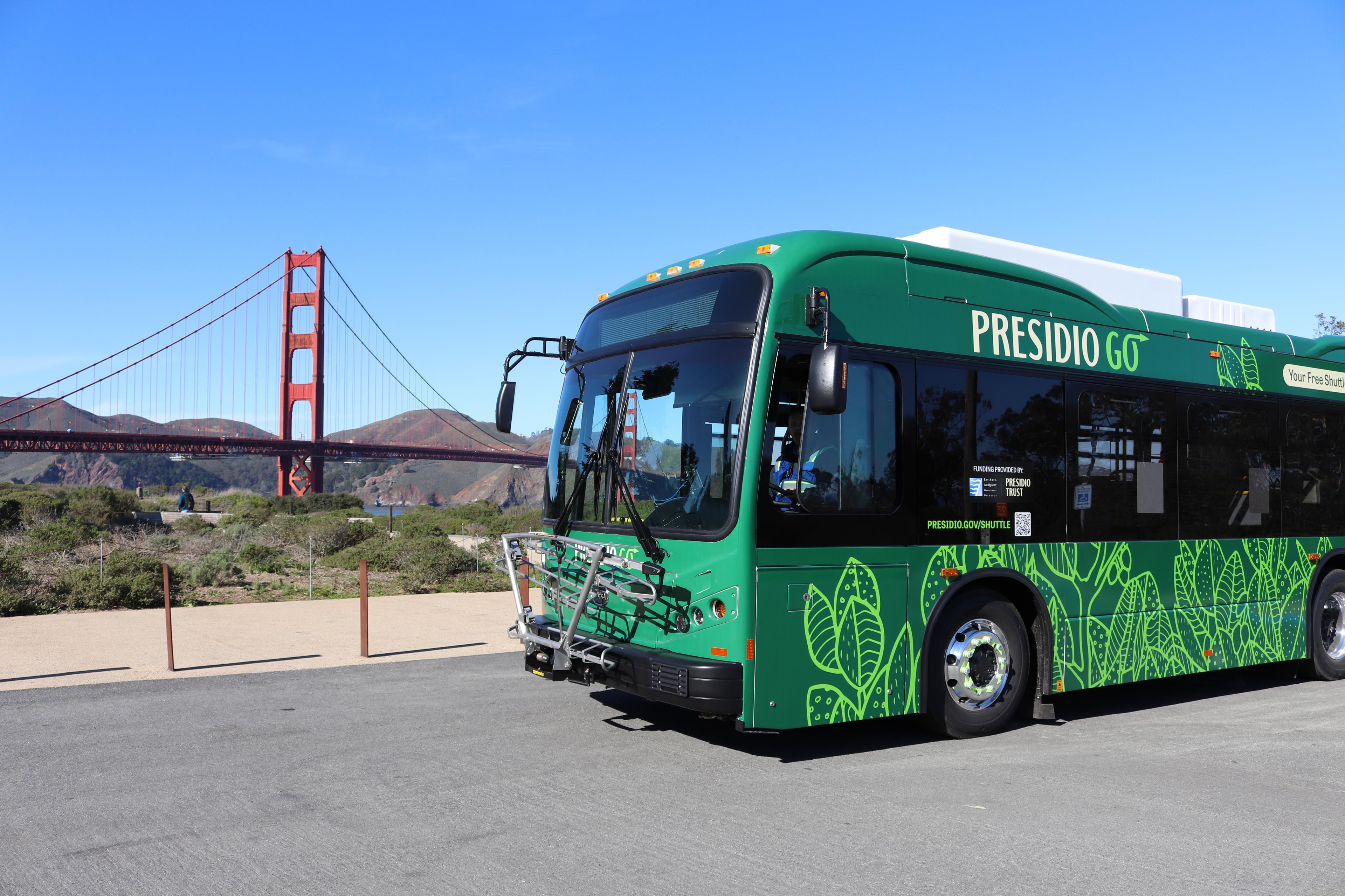 A green Presidio GO Shuttle with the Golden Gate Bridge in the background.