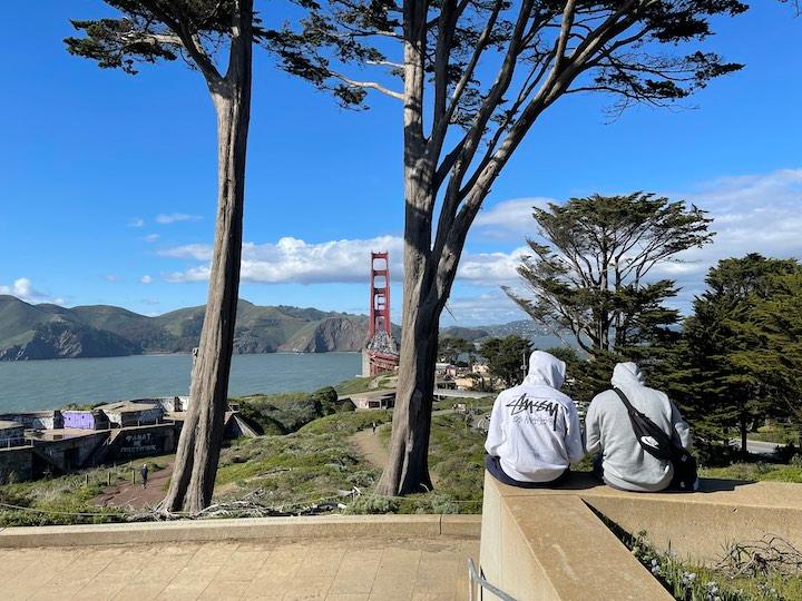 Golden Gate Overlook with two trees framing the bridge and two people sitting on the ledge talking.