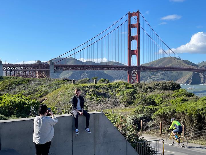 A woman takes a photo of a man with the Golden Gate Bridge at Battery East Vista in the Presidio.