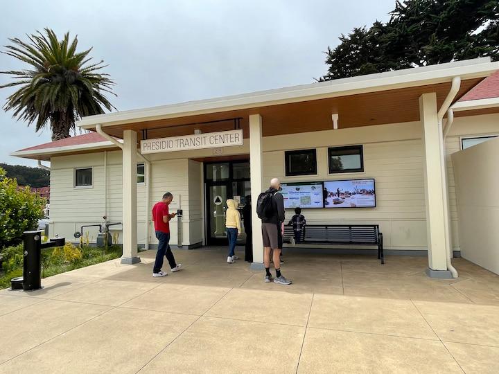 Several people standing outside Presidio Transit Center, some looking at digital kiosks.