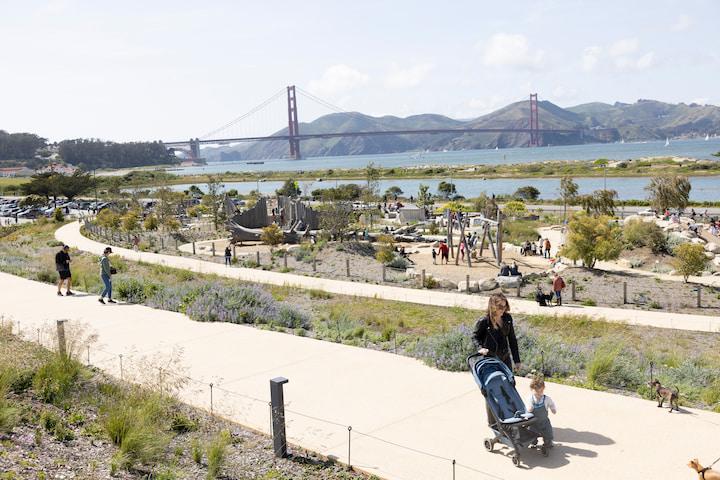 A woman with a stroller walks on a wide pathway at Presidio Tunnel Tops.