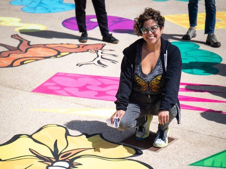 Favianna Rodriguez kneeling in front of her art mural at the Presidio. Photo by Alex Grant.