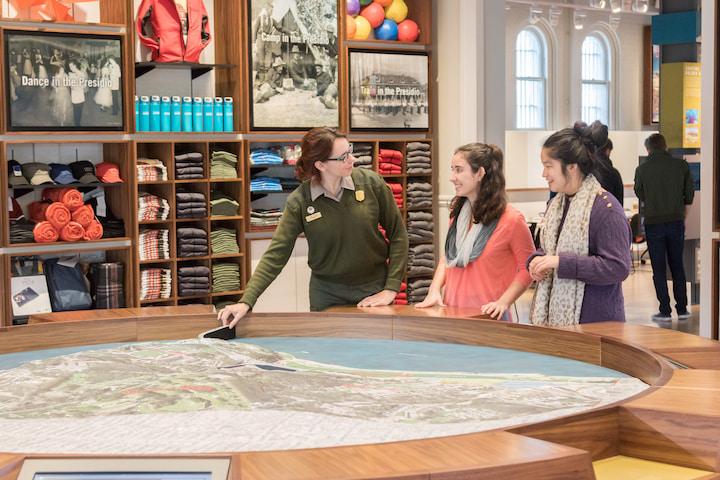 Interior of Presidio Visitor Center with a park ranger talking to two visitors near a map.