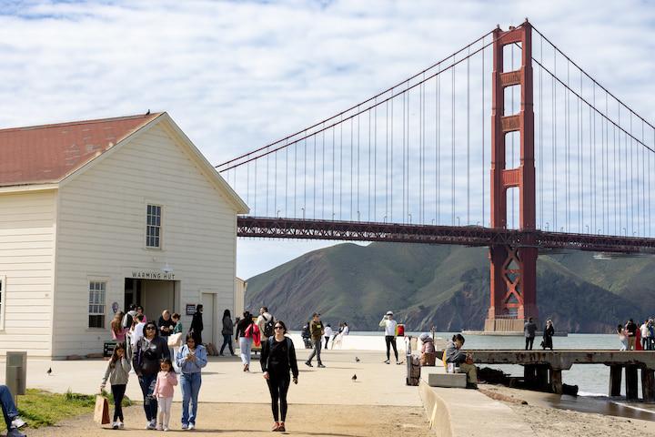 Visitors walk on a trail outside the Warming Hut, with the Golden Gate Bridge in the background.