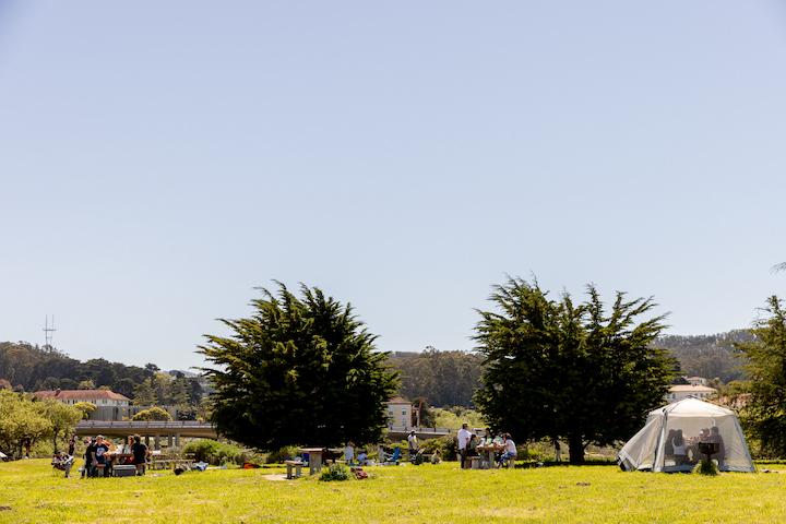 People gather at four picnic tables at Crissy Field East Beach. Photo by Myleen Hollero.