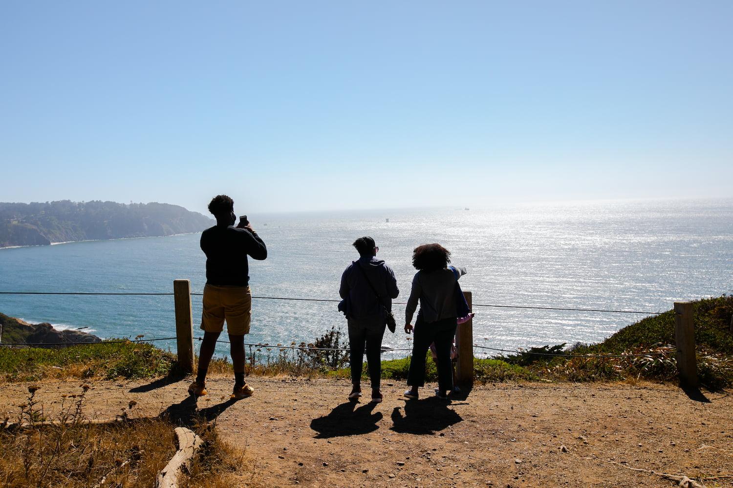 Three people taking a photo of the Golden Gate Bridge from the California Coastal Trail.