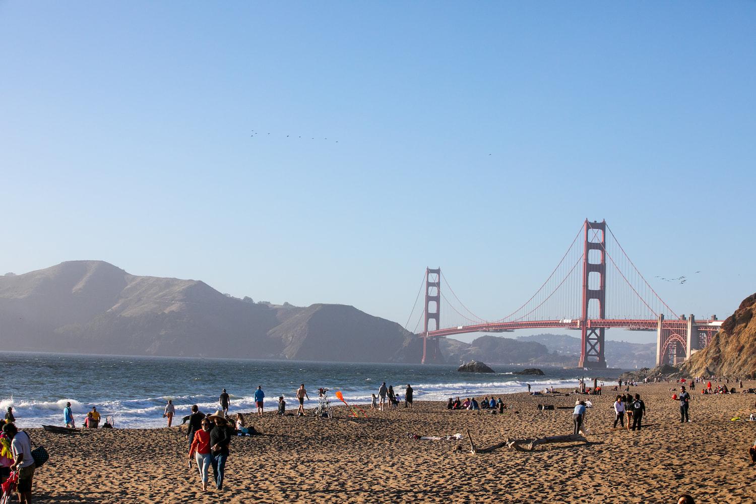 A dozen people walking or sitting on the sand at Baker Beach.