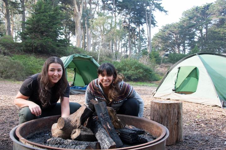 Two girls around a fire and near their tents