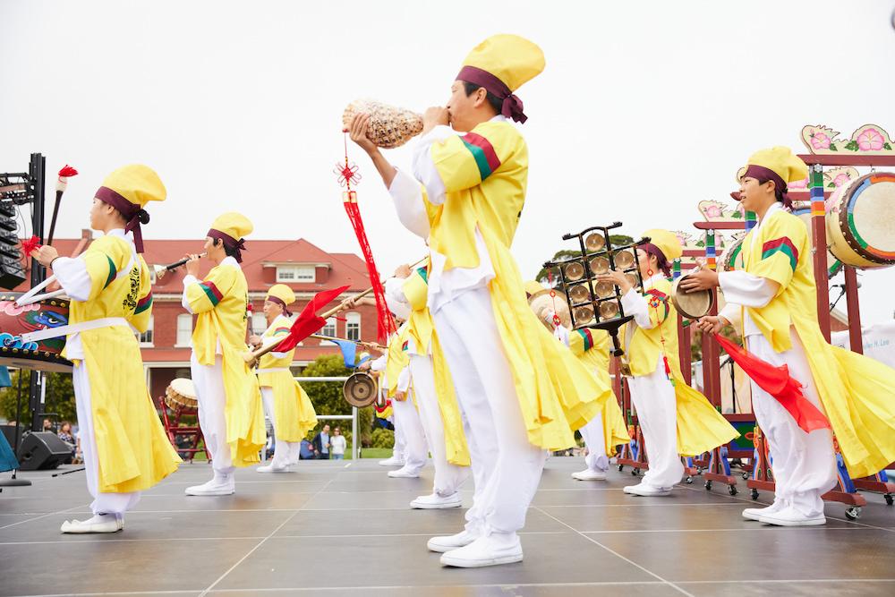 Image of a group performing in yellow outfits with instruments during the Chuseok Festival.