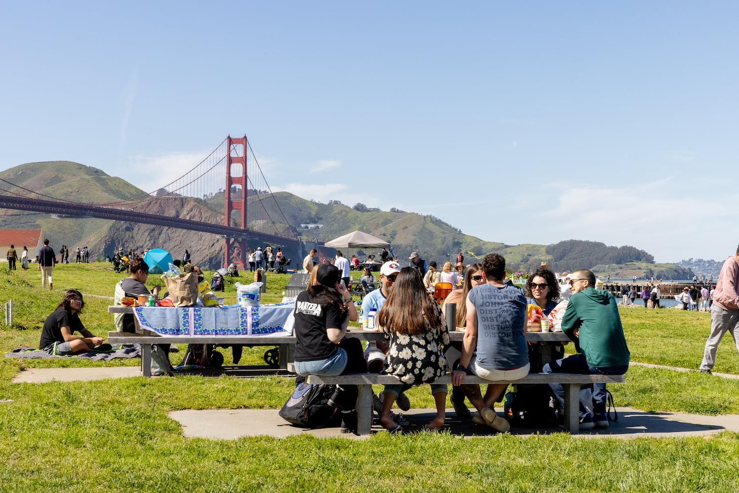 Visitors picnicking at Crissy Field West Bluffs with the Golden Gate Bridge in the background.